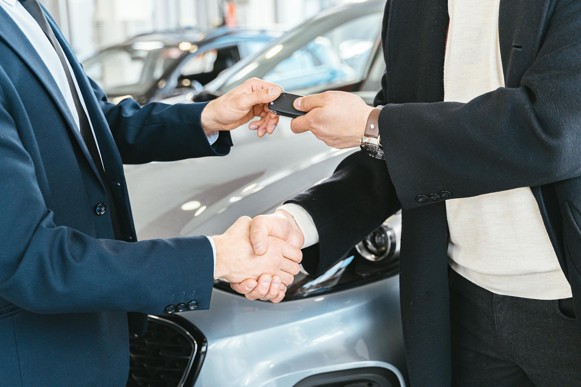 a person giving a car key to another person while shaking his hands